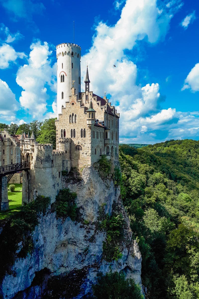 Beautiful Lichtenstein Castle perched on a cliff, surrounded by lush greenery, under a vibrant blue sky.