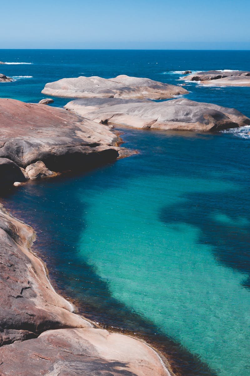 Clean blue water of tranquil water of ocean surrounded with stony terrain under cloudless blue sky
